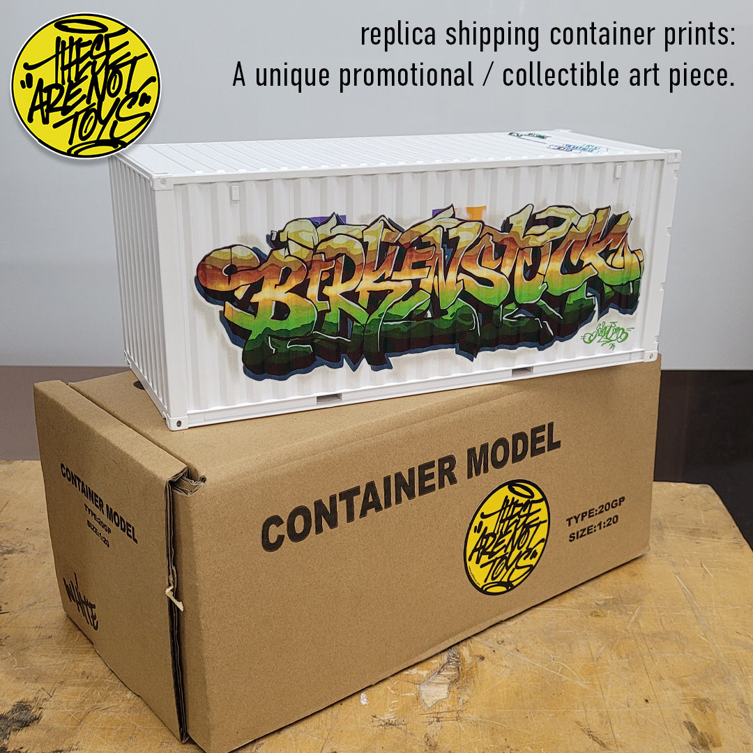 Replica shipping container with graffiti art and cardboard box labeled 'Container Model' on a wooden surface.